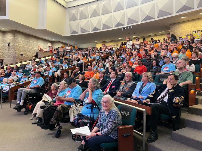 Rows and rows of seats are filled with residents, many wearing sky blue shirts that read "Build It Now" referring to a veterans cemetery. Others, wearing orange, want to stick to plans to build the cemetery in Anaheim.