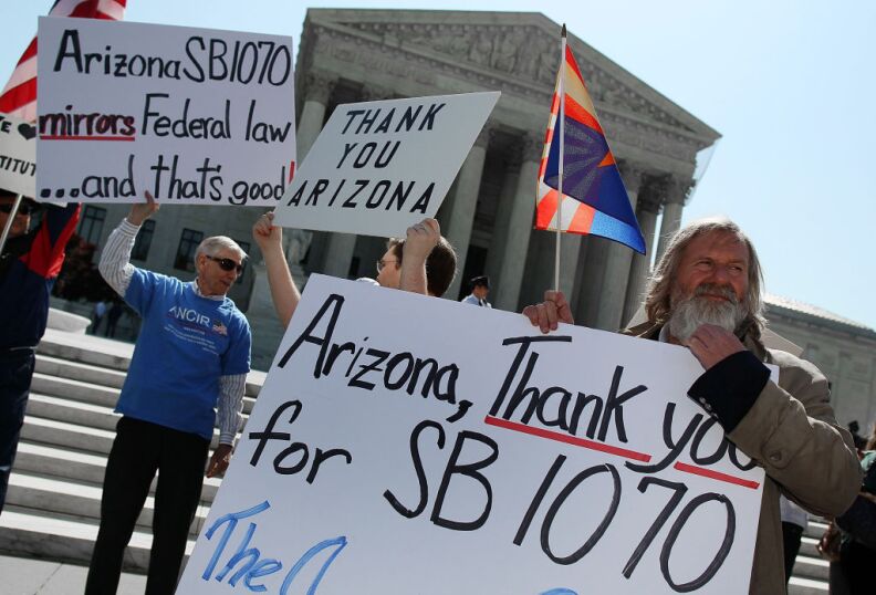 WASHINGTON, DC - APRIL 25: People protest in front of the U.S. Supreme Court, on April 25, 2012 in Washington, DC. Later this morning the high court will hear arguments on Arizona v. United States and will be tasked with deciding the conflicting roles of national and state governments in controlling the lives of noncitizens living illegally in the U.S. while deciding the constitutionality of Arizona's immigration law SB 1070.  (Photo by Mark Wilson/Getty Images)