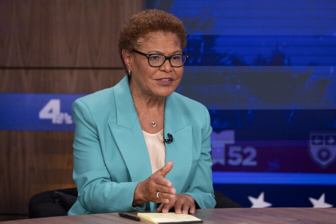 A Black woman sits at a news desk gesturing while speaking, with LMU and station logos on screens behind them.
