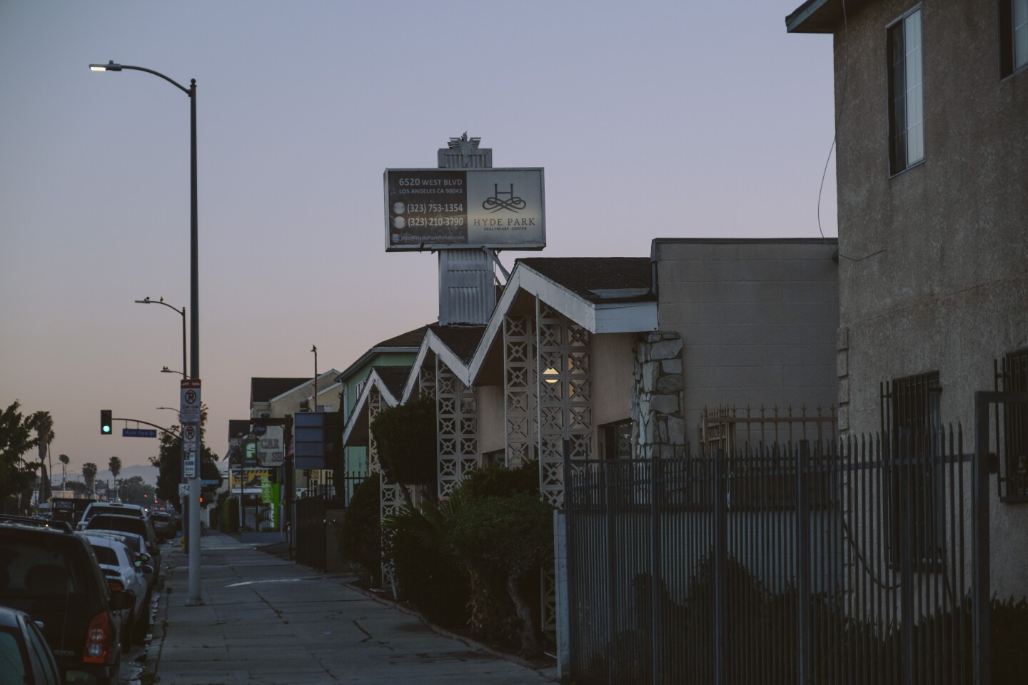 A view of Hyde Park Health Center at dusk. The mid-century building has a zig-zag roof and open cinderblock. The sign rises out of the roof.