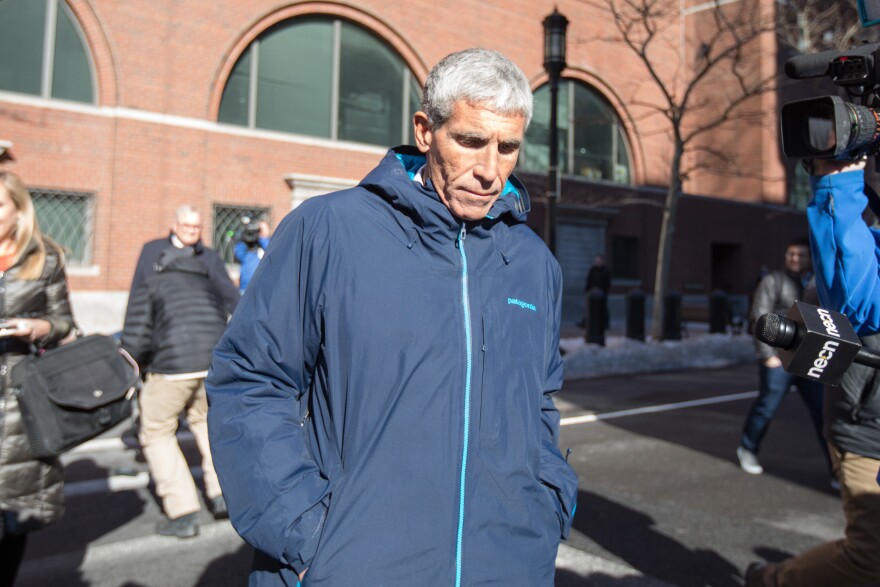 A gray-haired man with light-medium tone skin leaves a court in a blue windbreaker