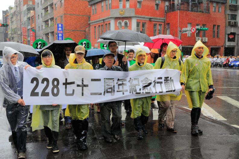 A group of protesters in rain coats march during a demonstration down a wet city street.
