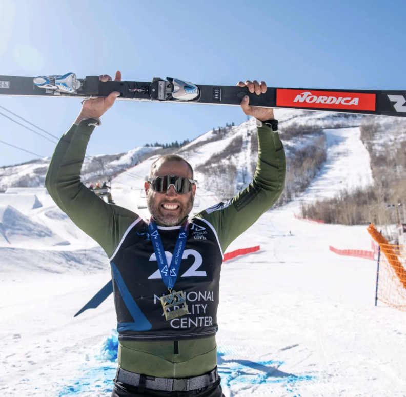 Competitive Alpine Skier Matthew Brewer holds a ski over his head while wearing a green shirt.