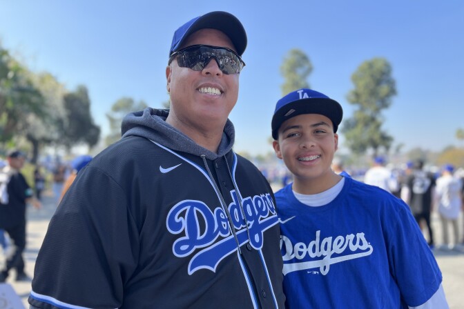 A man in his early 50s poses with a young teenage boy. Both are wearing Dodgers jerseys.