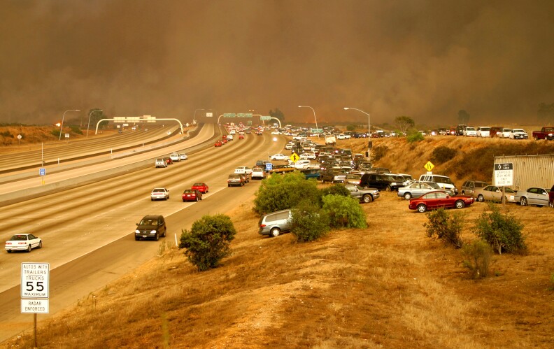 An ominous cloud of smoke in the background as cars pull chaotically off the freeway.