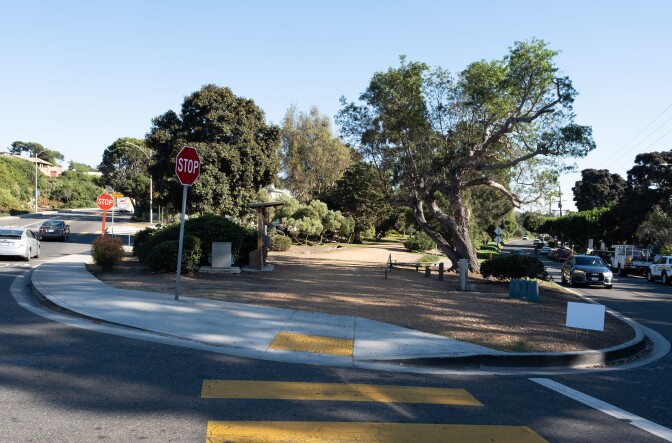 A street with cars and a wood chipped walking path with trees.