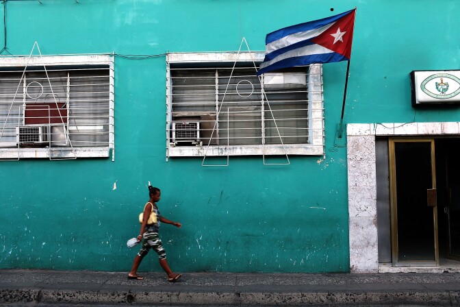 SANTIAGO DE CUBA, CUBA - MARCH 22:  A woman walks under a Cuban flag on March 22, 2012 in Santiago de Cuba, Cuba. Fourteen years after Pope John Paul II visited Cuba, Pope Benedict is scheduled to arrive into the communist country on Monday the 26th. Benedict, who will be arriving from Mexico, will conduct a mass in the city of Santiago de Cuba first followed by a mass in Havana before leaving on the 28th. Tensions are high in Cuba between dissidents and the government as activists hope the international exposure of the Papal visit will result in renewed attention to their struggle for greater freedoms.  (Photo by Spencer Platt/Getty Images)
