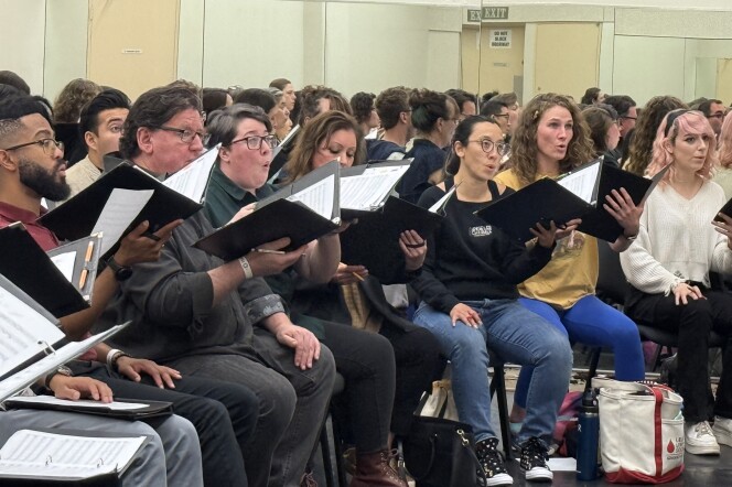 A group of more than a dozen singers with the Angeles Chorale rehearse at The Dorothy Chandler Pavilion. They hold binders filled with music notation. 