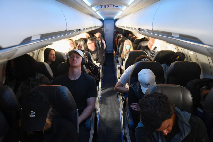 Airline passengers, some not wearing face masks, sit during a light