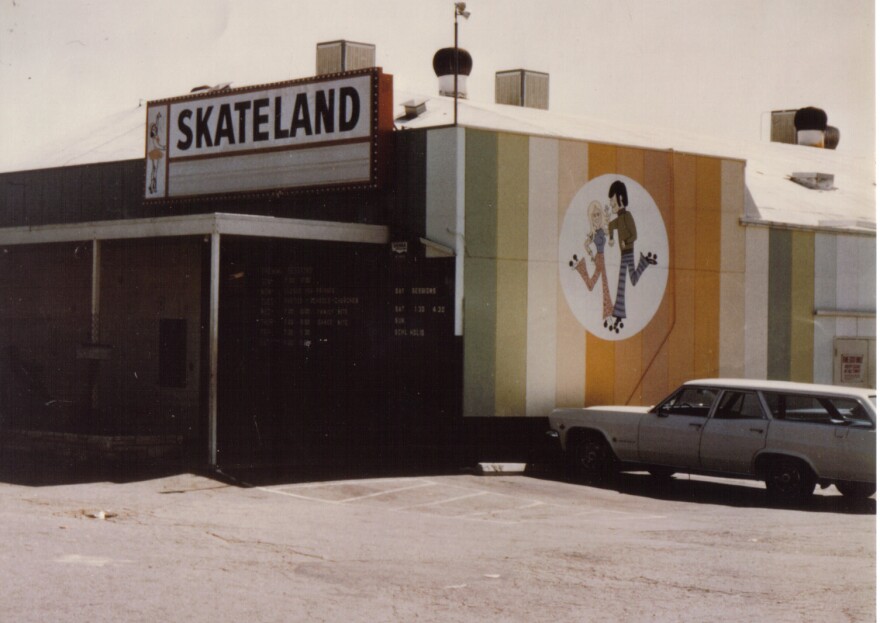 Skateland’s exterior is seen in a 1975 photo. One wall has many bands of stripes in different, muted colors.
