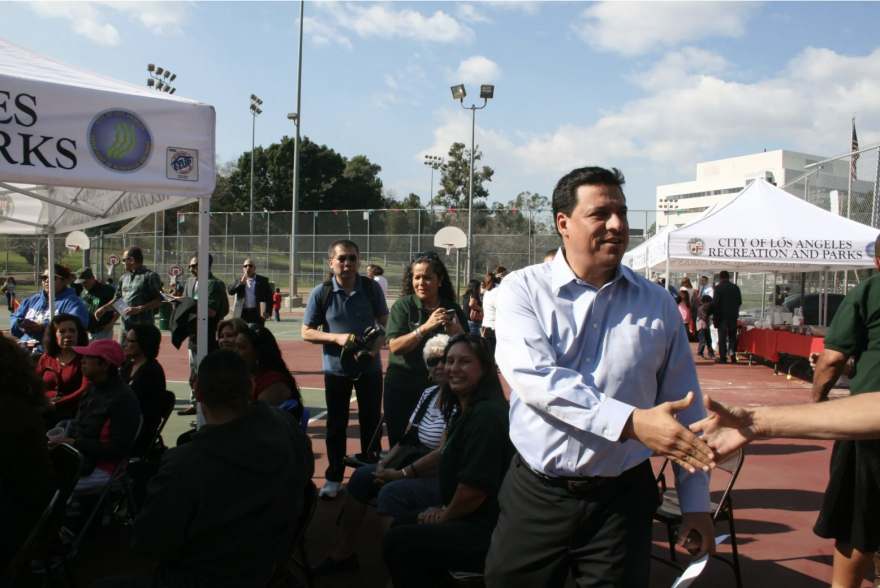 A brown-skinned man shakes hands with people in a crowd during a campaign stop.