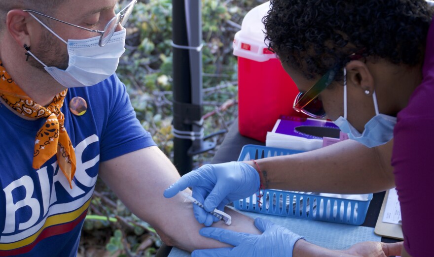A man receives a monkeypox vaccine on the inside of his forearm, as a health worker leans over his hand and administers the shot.
