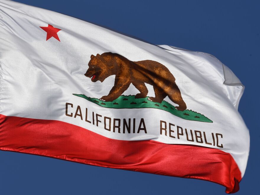 The state flag of California, featuring a grizzly bear, waves in the wind.