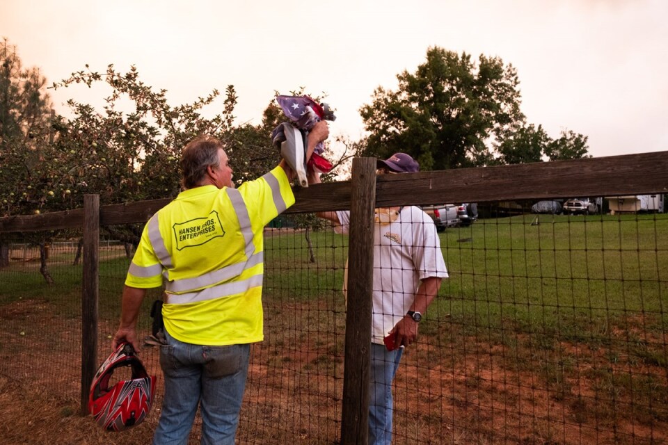 A man hands a U.S. flag to another man over a metal mesh fence