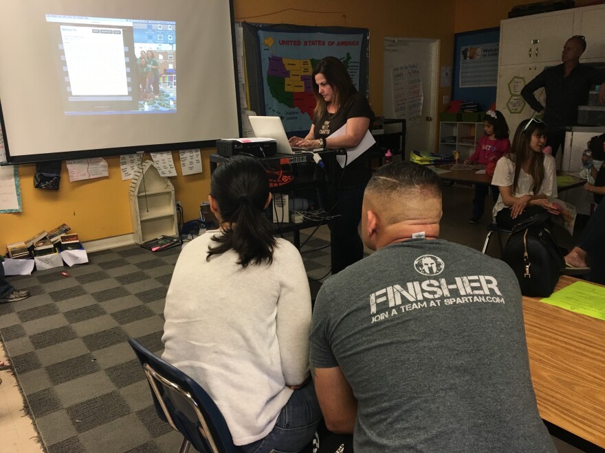FILE - Parents watch as a charter school principal conducts a lottery to determine which of the 257 applications will receive one of the 28 open slots in the school's kindergarten class.