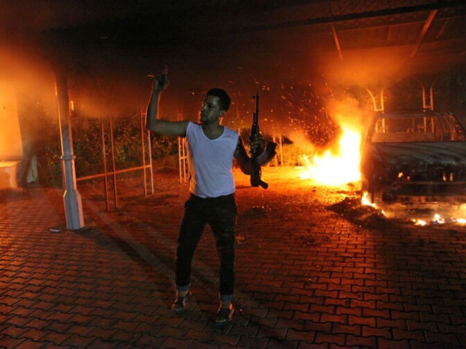 An armed man waves his rifle as buildings and cars are engulfed in flames after being set on fire inside the U.S. consulate compound in Benghazi late on Sept. 11, 2012. An armed mob protesting over a film they said offended Islam, attacked the U.S. consulate in Benghazi and set fire to the building, killing one American, witnesses and officials said.