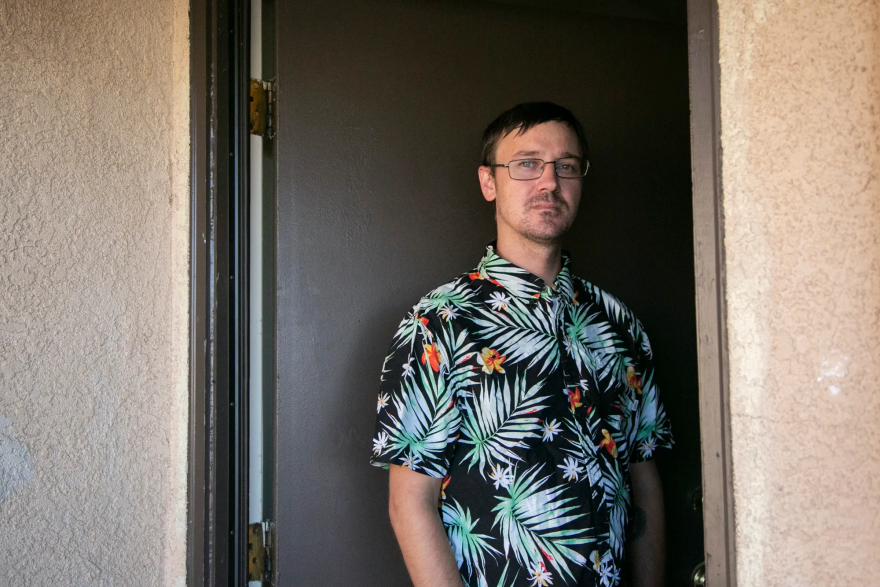 A man in a colorful shirt stands in an open doorway.
