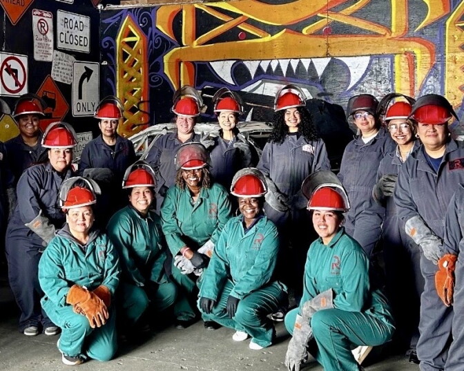 Female presenting people wear red constuction hats, gloves, and thick overalls.