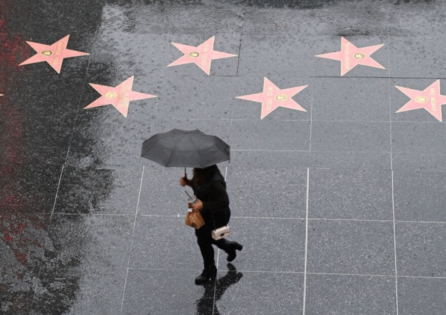 An ariel view of someone holding a Black umbrella walking on a wet Hollywood Walk of Fame.