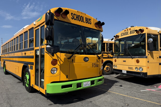 A yellow bus with a green fender. Black letters above the windshield read "SCHOOL BUS." 
