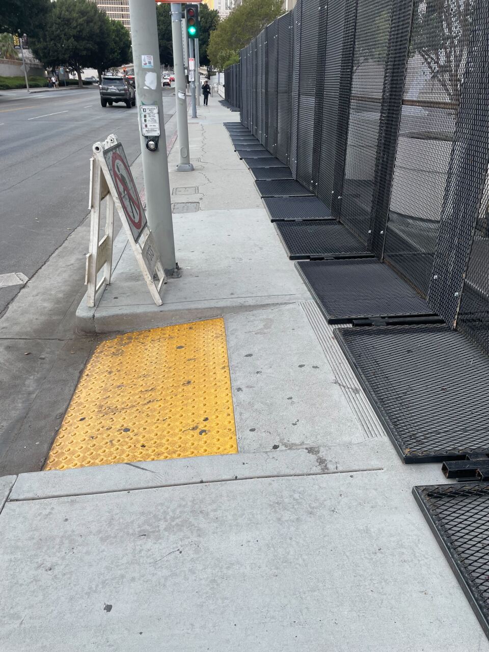 A portion of sidewalk with black metal fencing on the right side. A pedestrian onramp in the foreground leads up to the fencing. A "no pedestrian" sign is visible near the onramp.