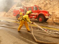RUNNING SPRINGS, CA - OCTOBER 24:  A San Bernardino City firefighter pulls a section of hose as firefighters try to prevent an out of control fire from jumping highway 18 October 24, 2007 in Running Springs, California. Nearly 500,000 people have been evacuated across the Southern California region and over 1,300 homes have been destroyed as wild continue to burn out of control in several southern California counties.  (Photo by Justin Sullivan/Getty Images) 