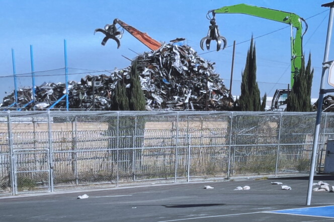 Two industrial waste machines can be seen from the blacktop at Jordan High School in Watts. Two massive claws hover over large piles of metal waste. 