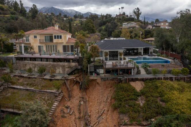 Two multi-story homes on the side of a hill bear damage from a mudslide behind their backyards.