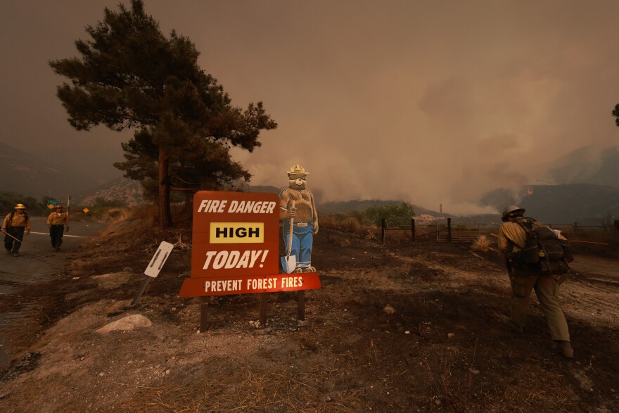 Firefighting personnel walk by a Smokey the Bear forest service sign warning of high fire danger