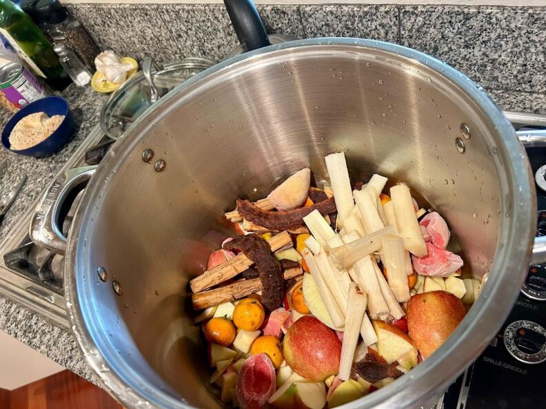 A metal pot on a stove with cut up fruit inside.