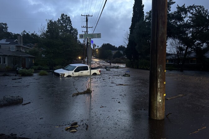 A white truck is submerged in solid mud near a street sign in a neighborhood