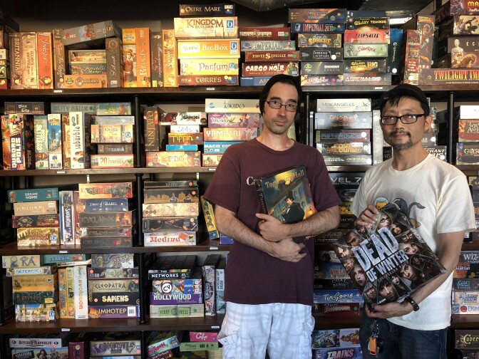 Game Haus co-owner Rob Cron and Terry Chiu holding two of their favorite games - Tammy Hall and Dead of Winter.