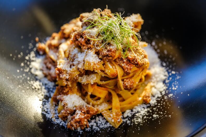 A bowl of long thick pasta noodles covered in parmesan cheese and green leaves.
