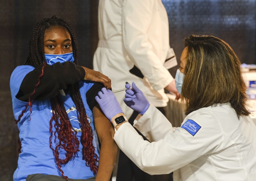 A young woman wearing a blue shirt gets a shot in her arm from a woman wearing a lab coat