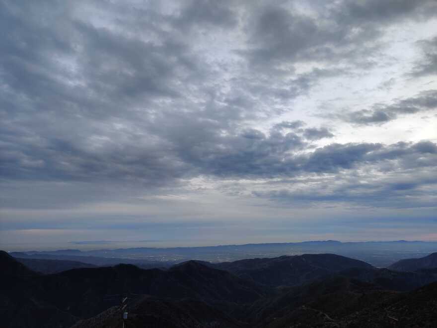 Storm clouds sweep the sky over rolling hills into a valley.