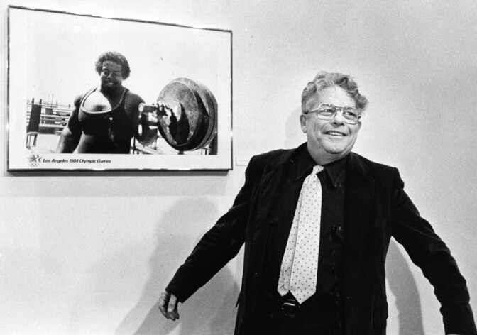 Photographer Garry Winogrand and his Olympics poster, featuring Venice bodybuilder William Pettis. Winogard stands in front of his poster of a weightlifter whose huge upper torso echoes the massive barbells at his side. Robert Fitzpatrick, head of the '84 arts festival, says he had in mind a poster series "that would not come all from a single sort of viewpoint." Photo dated: February 13, 1983. 
