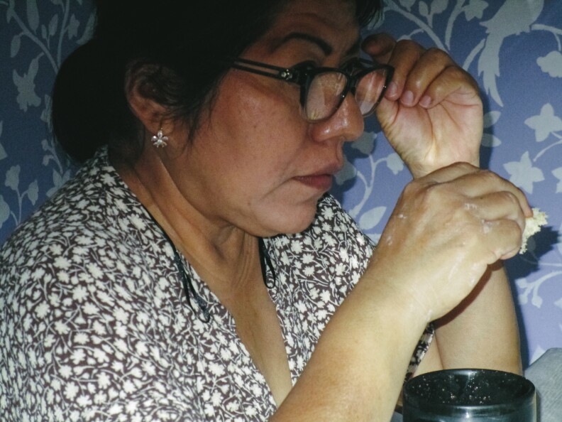This is an image of Luz Hernandez holding a small piece of bread directly over her coffee mug.