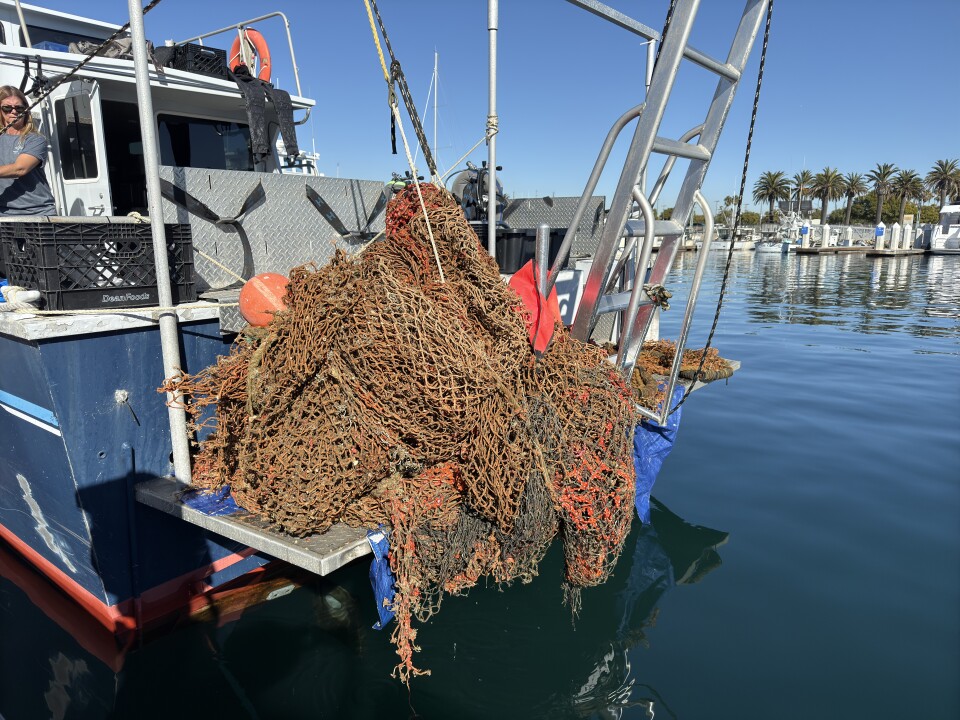 A large wad of fishing net on the back of a white and blue boat in a calm harbor on a sunny day. 