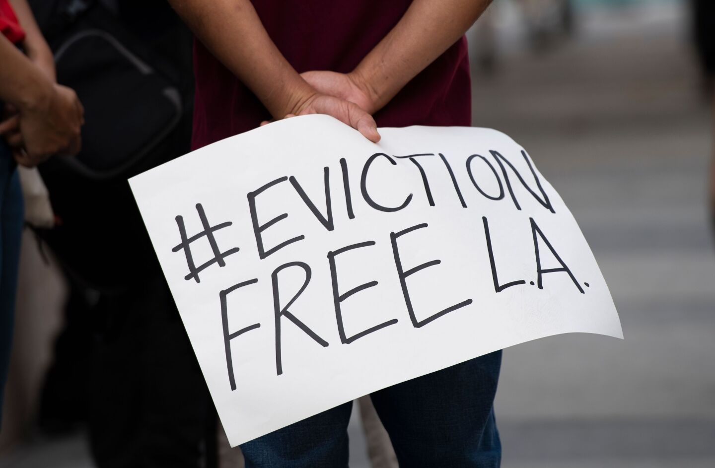 A person holds a handwritten sign on a poster board that reads: # Eviction Free L.A.