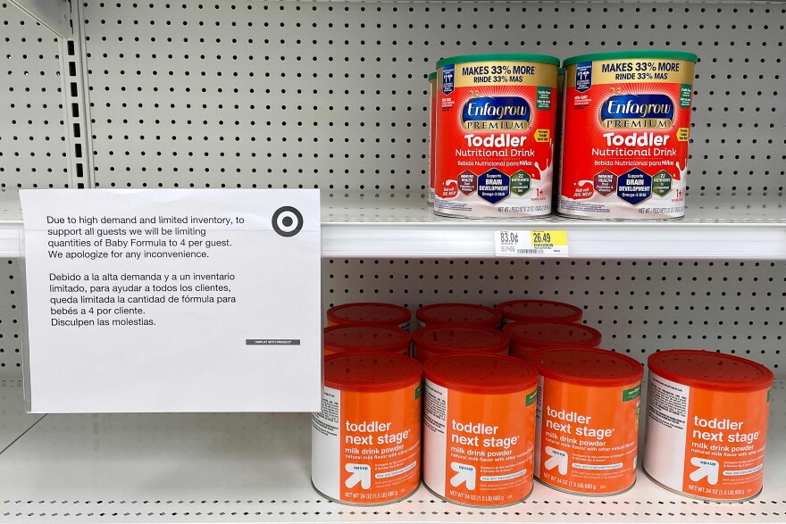 Store shelves are half empty, with several containers of toddler nutritional drink mix next to a sign noting a shortage of similar products.