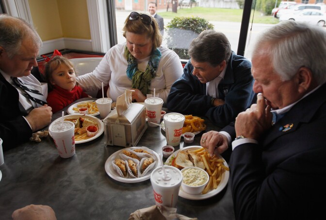FLORENCE, SC - JANUARY 17:  Republican presidential candidate, Texas Gov. Rick Perry (2nd R) bows his head in prayer with Kevin Rawlinson (L-R), Ella Rawlinson, Stephanie McLaughlin Rawlinson and Medal of Honor recipient, Michael Thornton, before they eat lunch during a campaign visit to the Drive-In restaurant on January 17,2012 in Florence, South Carolina. Perry continues to campaign for votes in South Carolina ahead of the  primary on January 21st.  (Photo by Joe Raedle/Getty Images)