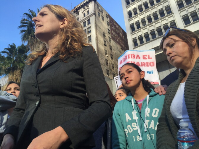 Attorney Emi MacLean of the National Day Laborers Organizing Network speaks at a rally for Romulo Avelica-Gonzalez. His daughter Fatima, middle, looks on. Avelica was detained for deportation after living in the U.S. for 25 years, according to his attorney.