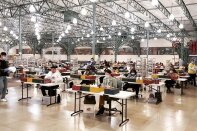 Election workers in a warehouse sit at voting tables and process votes