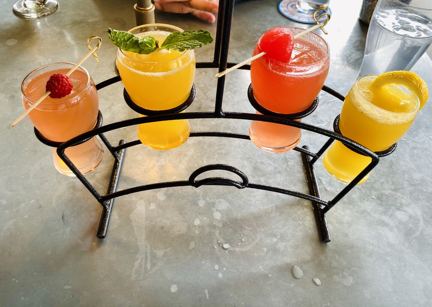 four glasses of orange liquid sit in an arched metal rack