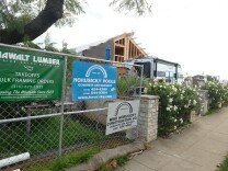 Fencing lines a sidewalk next to a home under construction. Signs on the fence bear the Horusicky name.