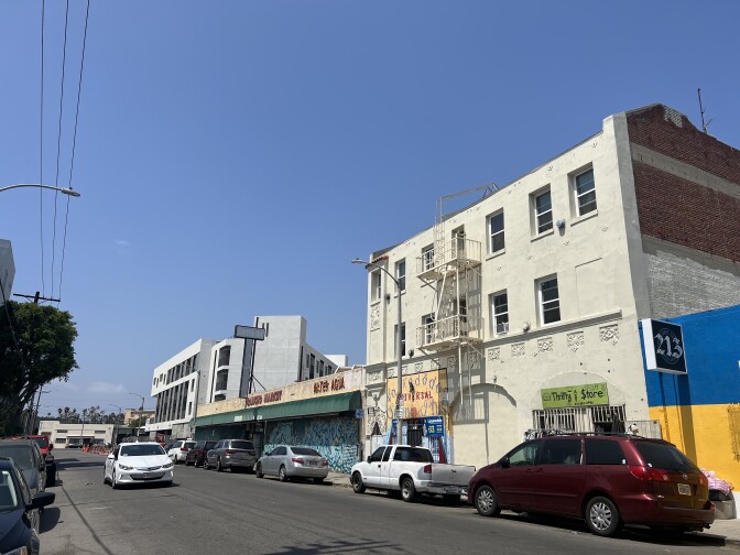 A street with several cars parked on each side. There's a mix of old buildings and new construction in this corridor. 