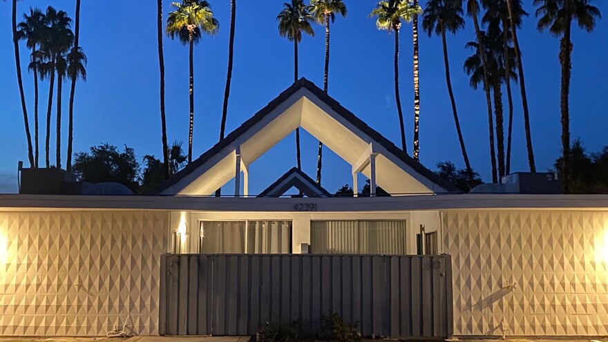 Dimly lit mid-century Palm Springs home with palm trees in the background