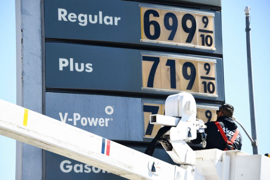 A worker in a bucket changes out the prices on a gas station sign.