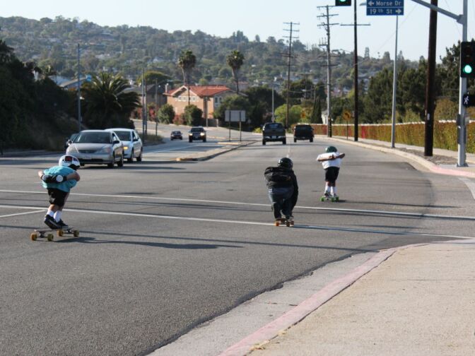 Three boys pass through an intersection as they skate down Western Ave.
