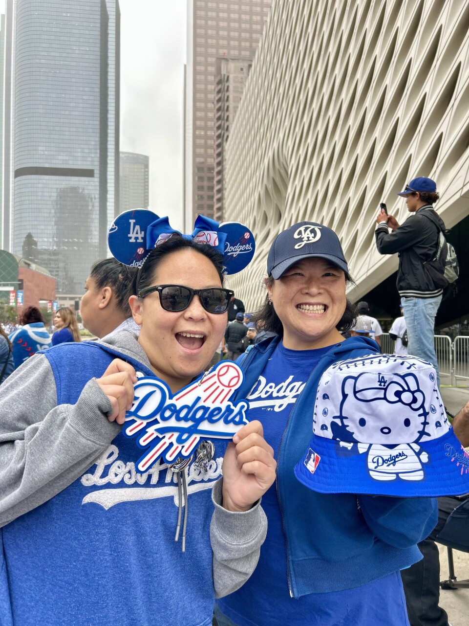 Two women, one wearing blue Minnie ears and another a Dodgers hat, smile holding Dodger gear. 